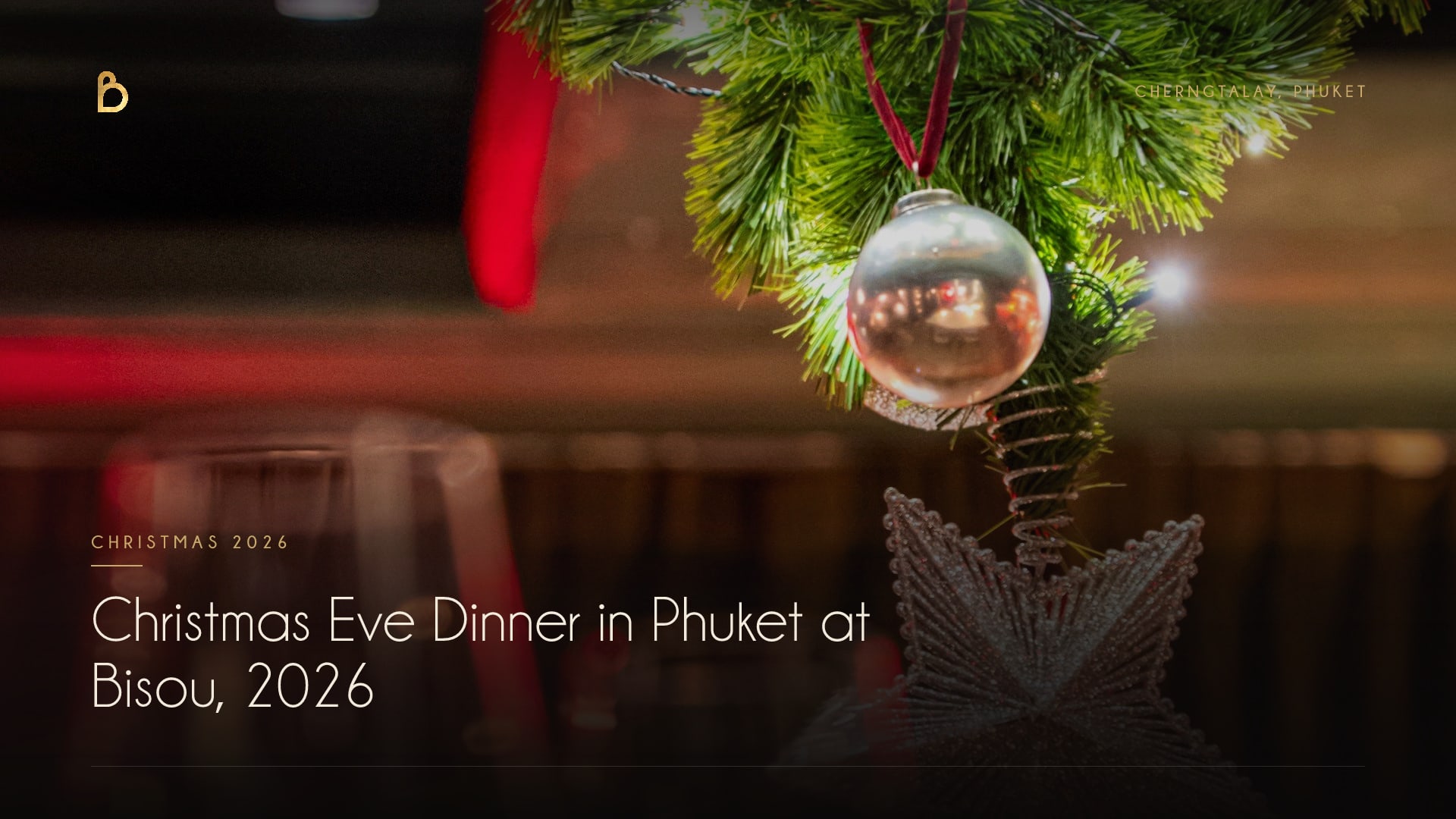 A silver bauble on a red ribbon and a glittering star hanging from the tip of a Christmas tree, with wine glasses blurred behind